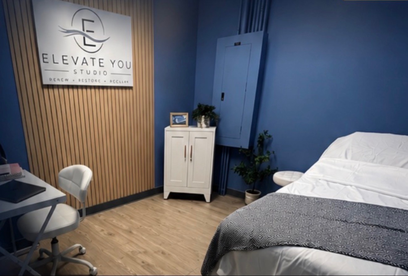 Treatment room at Elevate You Studio in Glasgow with the studio sign above a wood slat wall and a made treatment table